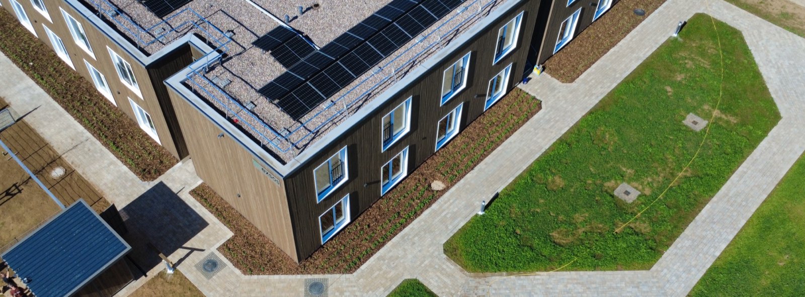 Luftaufnahme von exsos55 in Schenklengsfeld: zweigeschossiger Holzbau mit Photovoltaik auf dem Dach, gepflasterte Wege und Rasenflächen